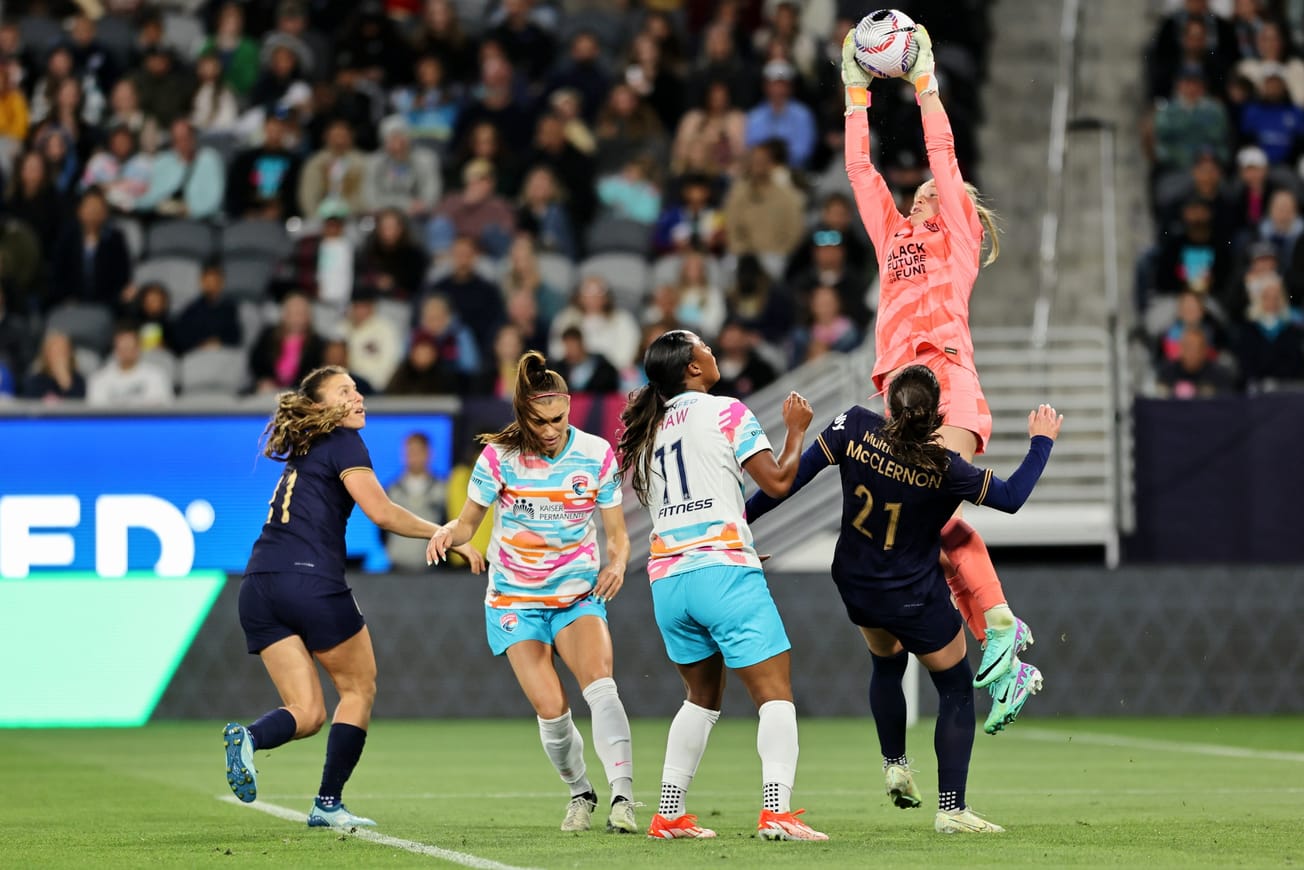 Reign goalkeeper Claudia Dickey leaps to claim a ball above several teammates and San Diego opponents.