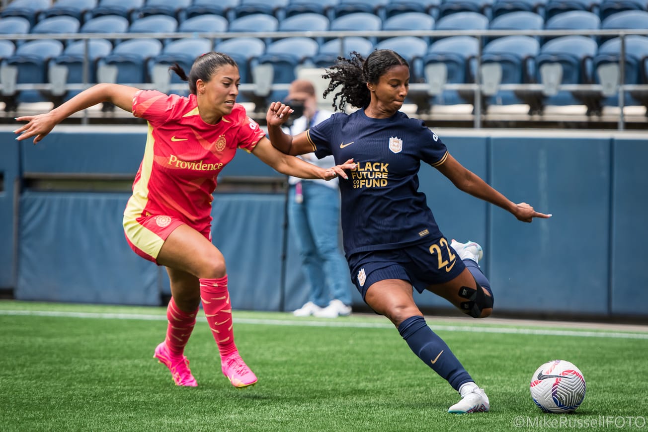 Reign defender Ryanne Brown lines up a cross as she fends off a challenge by a Thorns player in June 2024.