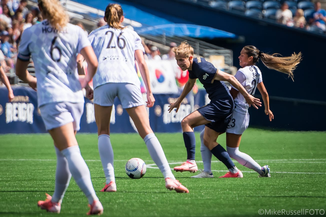 Reign midfielder Quinn dribbles against several Racing Louisville players in a June 2024 match.