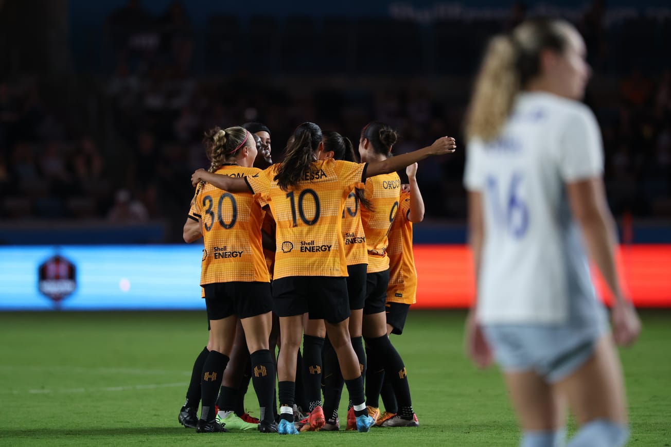 Houston Dash group hug to celebrate Yuki Nagasato's goal, with Jaelin Howell out of focus in the foreground
