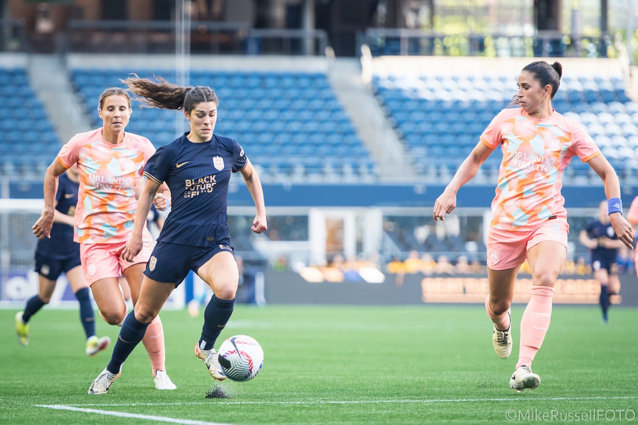 Reign forward McKenzie Weinert dribbles against two Orlando Pride players in a May 2024 match.
