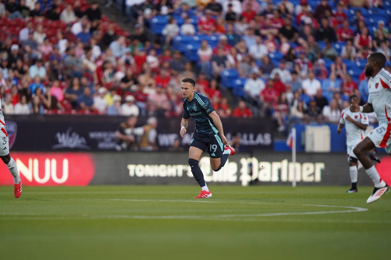 Danny Musovski wearing a navy blue Sounders kit running on a soccer field.