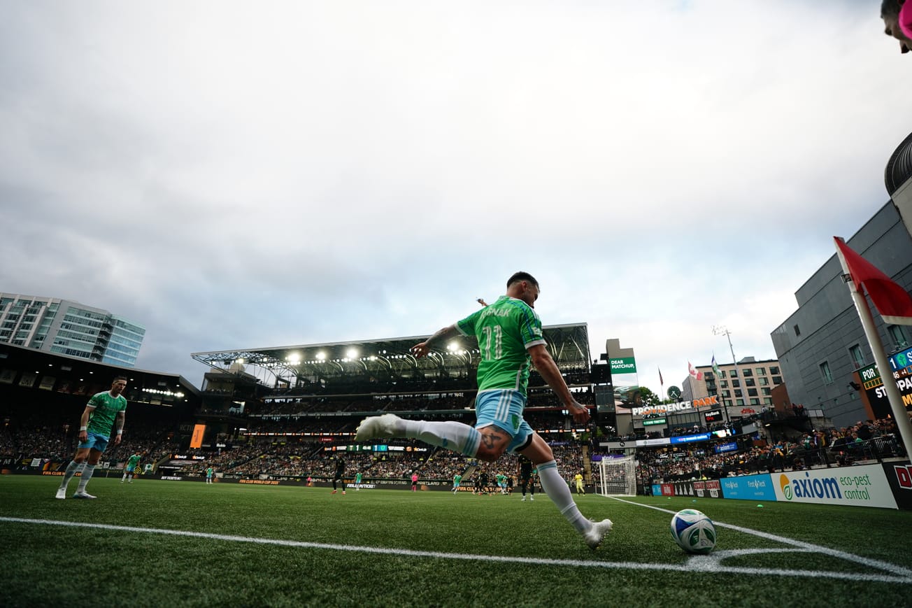 Albert Rusnák wearing a green Sounders jersey with the number 11 on the back and blue shorts taking a corner kick.