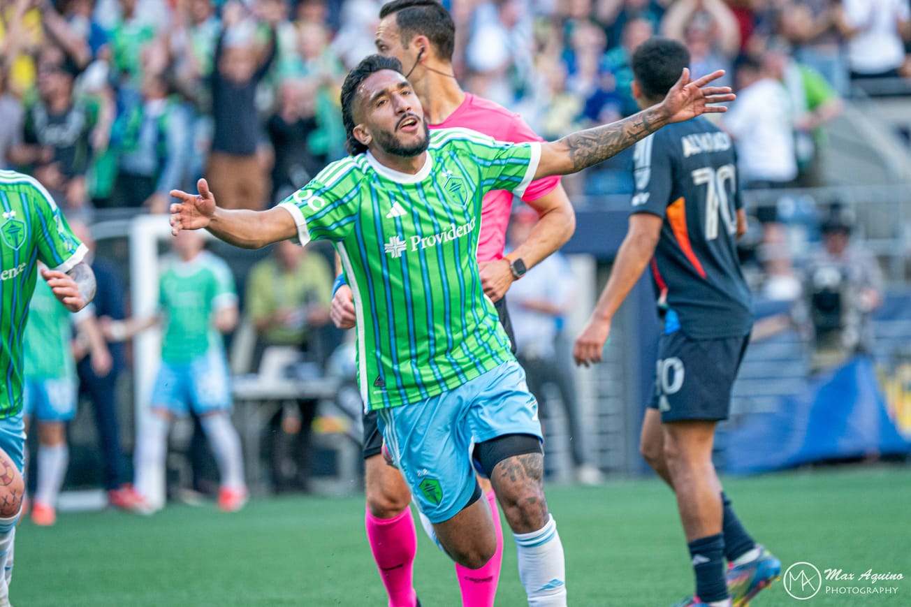 Jesus Ferreira wearing a green Sounders jersey and light blue shorts celebrates scoring a goal with his arms outstretched