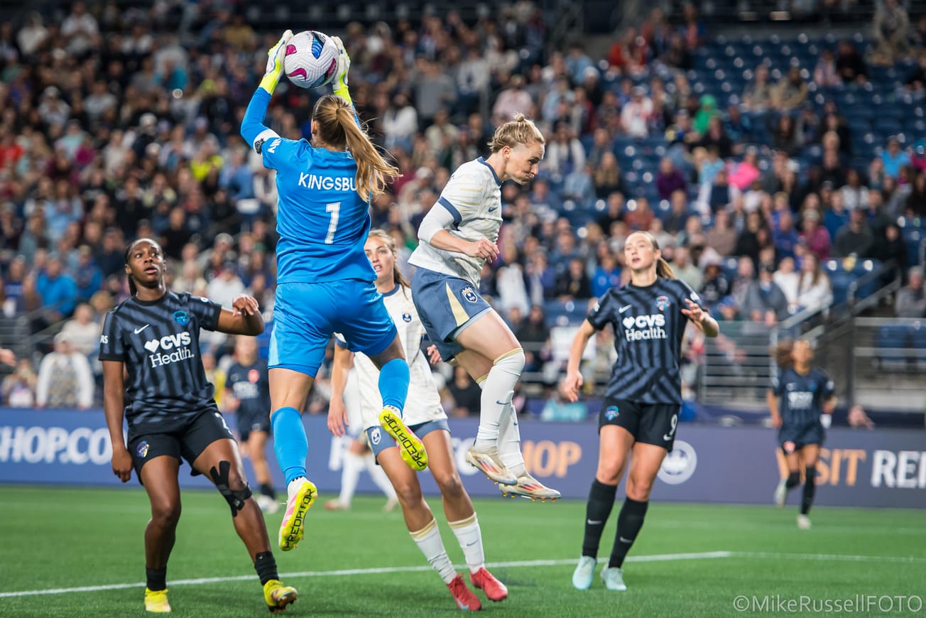 Reign midfielder Jess Fishlock attempts to challenge for a ball against Washington Spirit goalkeeper Aubrey Kingsbury in a May 2025 match.