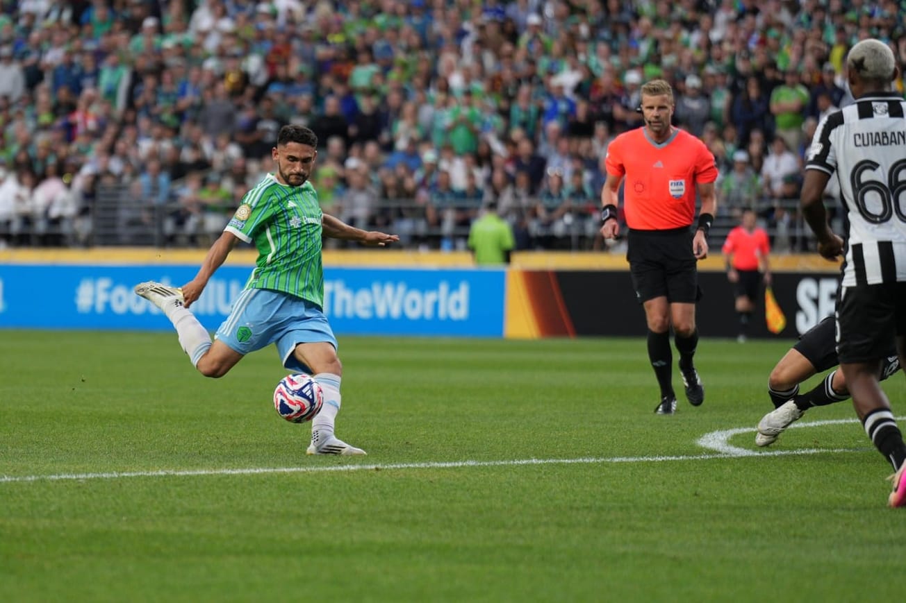 Cristian Roldan in a green Sounders jersey with light blue shorts swings to kick a ball