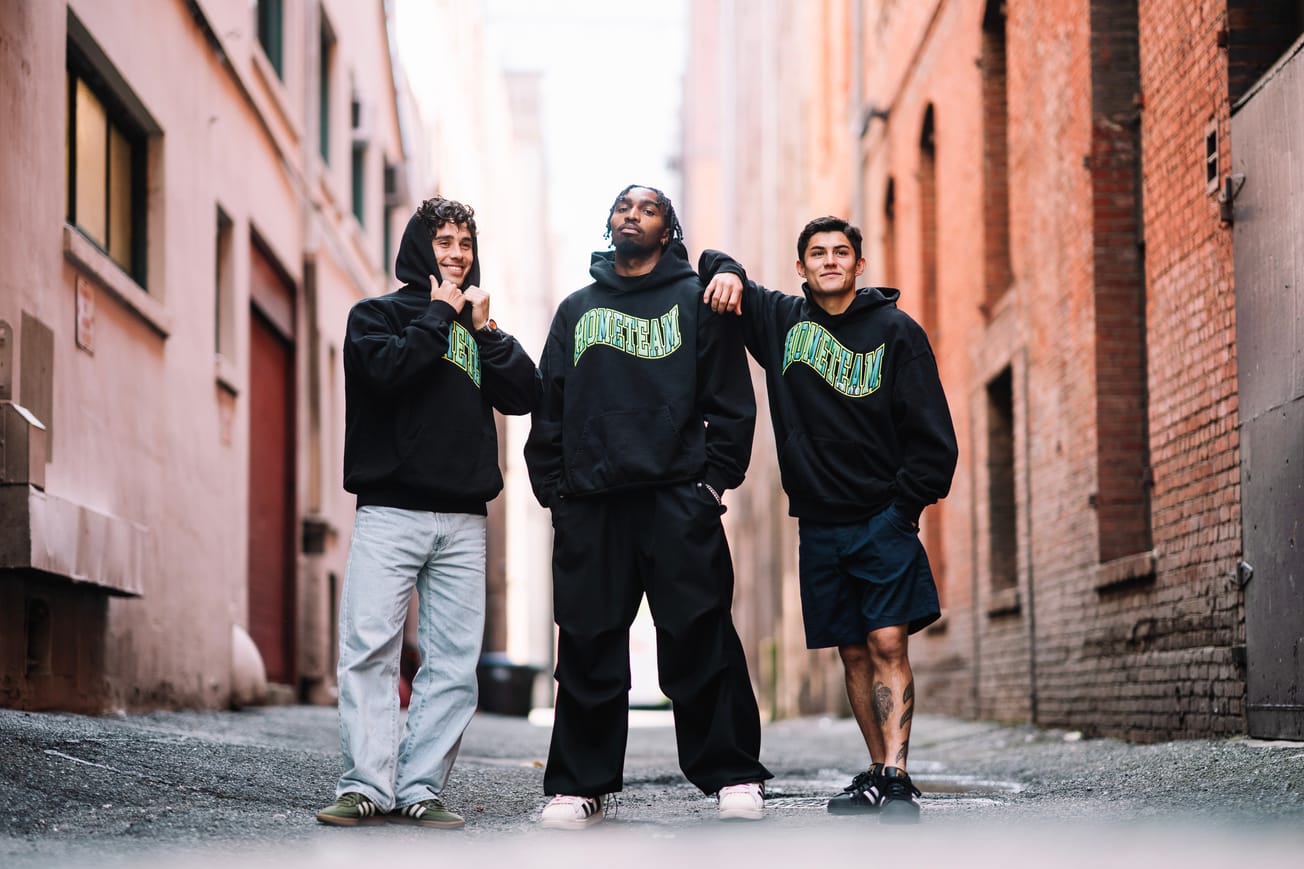 Paul Rothrock, Jon Bell and Kalani Kossa-Rienzi stand in an alley wearing black hooded sweatshirts with waves “HOMETEAM” text across the chest.