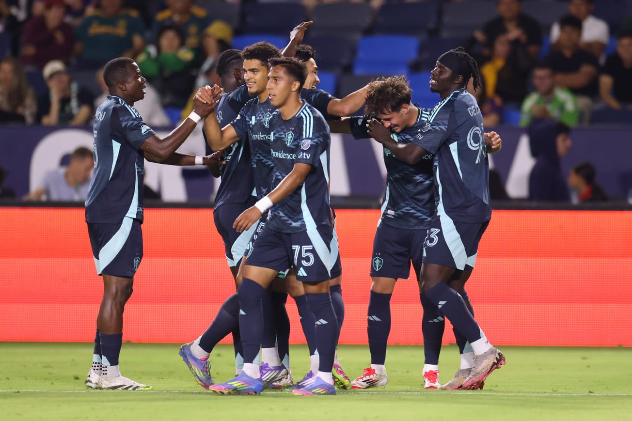 Sounders players in blue kits celebrate with Snyder Brunell after his goal.