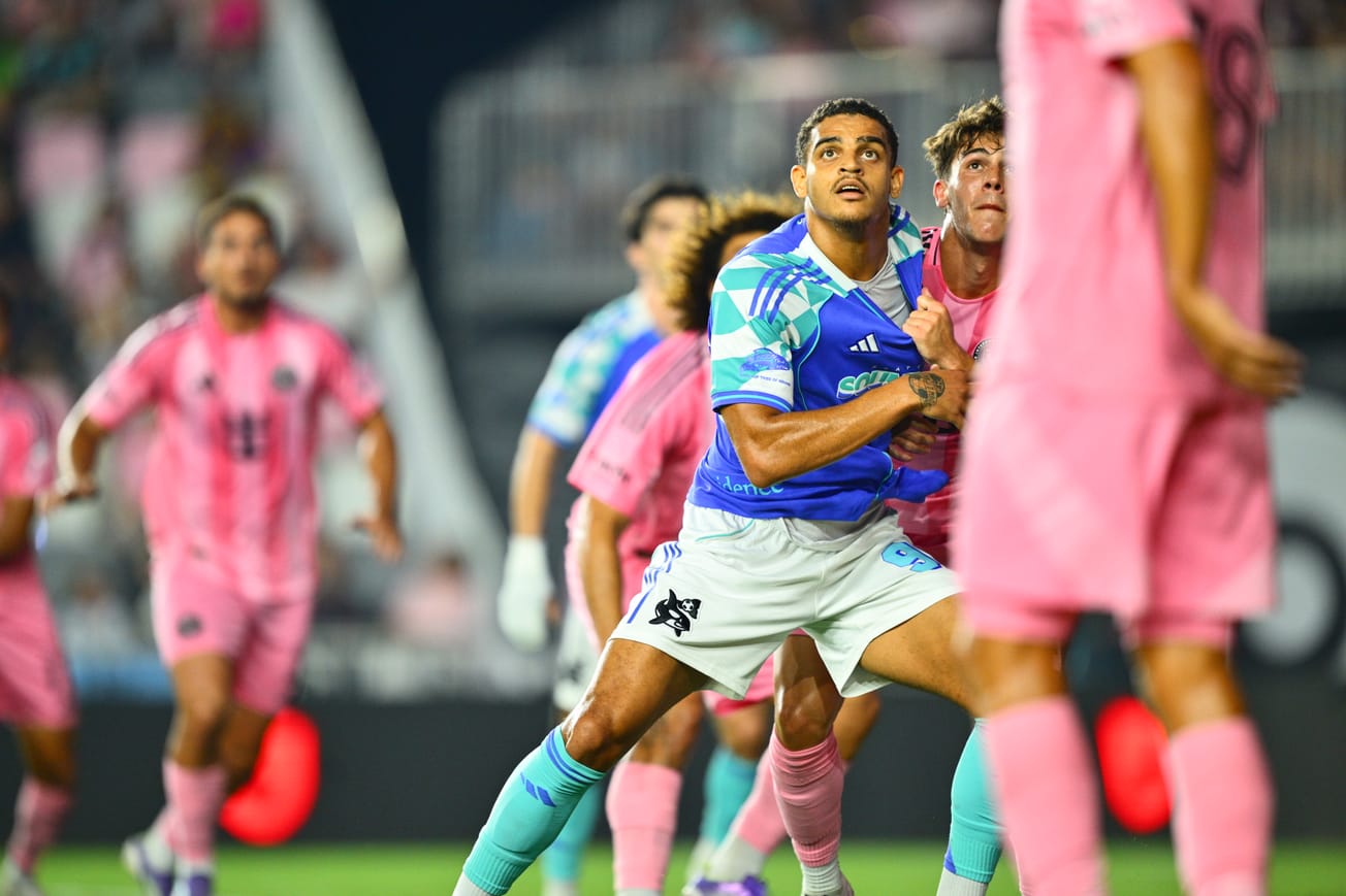 Osaze De Rosario in a blue Sounders kit has his jersey pulled by a Miami defender in a pink k