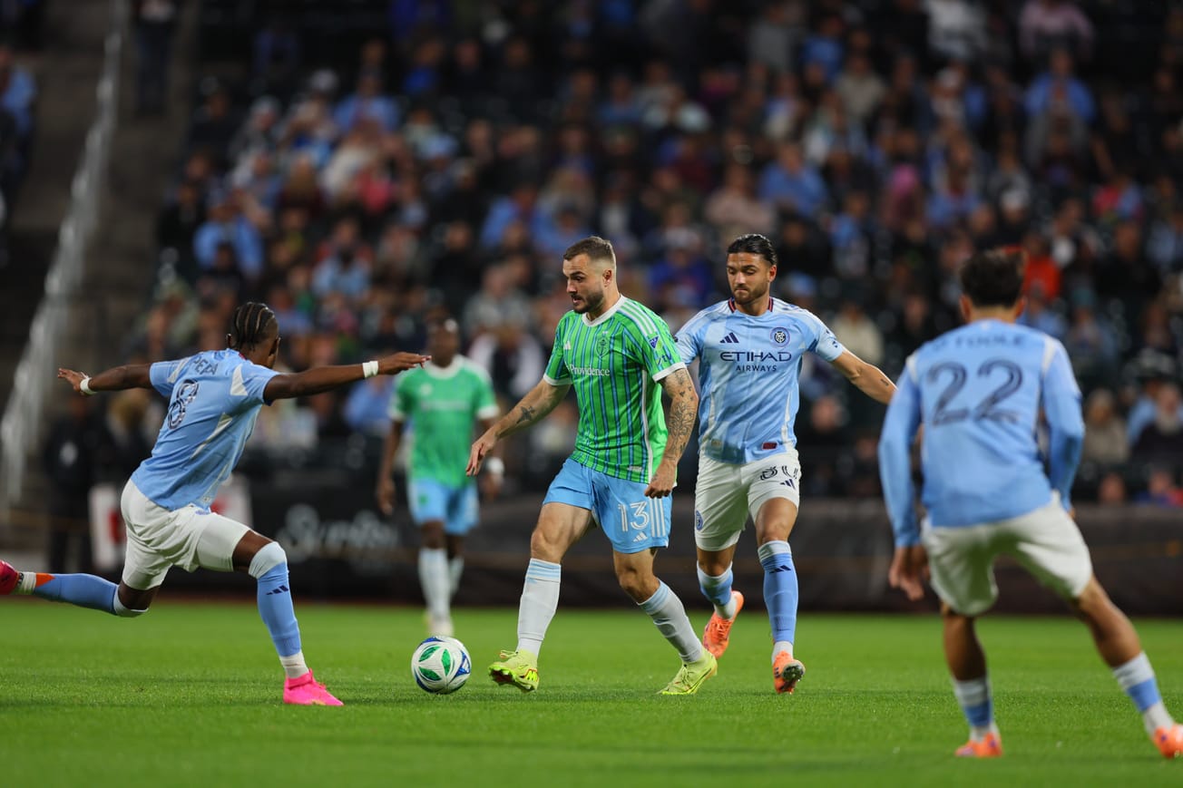 Jordan Morris in a green Sounders jersey and blue shorts dribbles surrounded by defenders