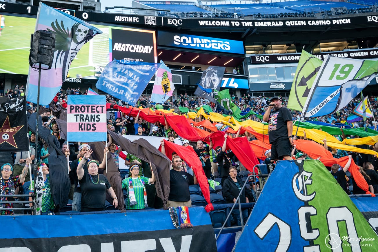 ECS members hold up flags including “Protect Trans Kids”, “Anti-Fascist, Anti-Racist, Always Seattle” and the Iron Front flag during the team’s annual Pride Match in 2025.